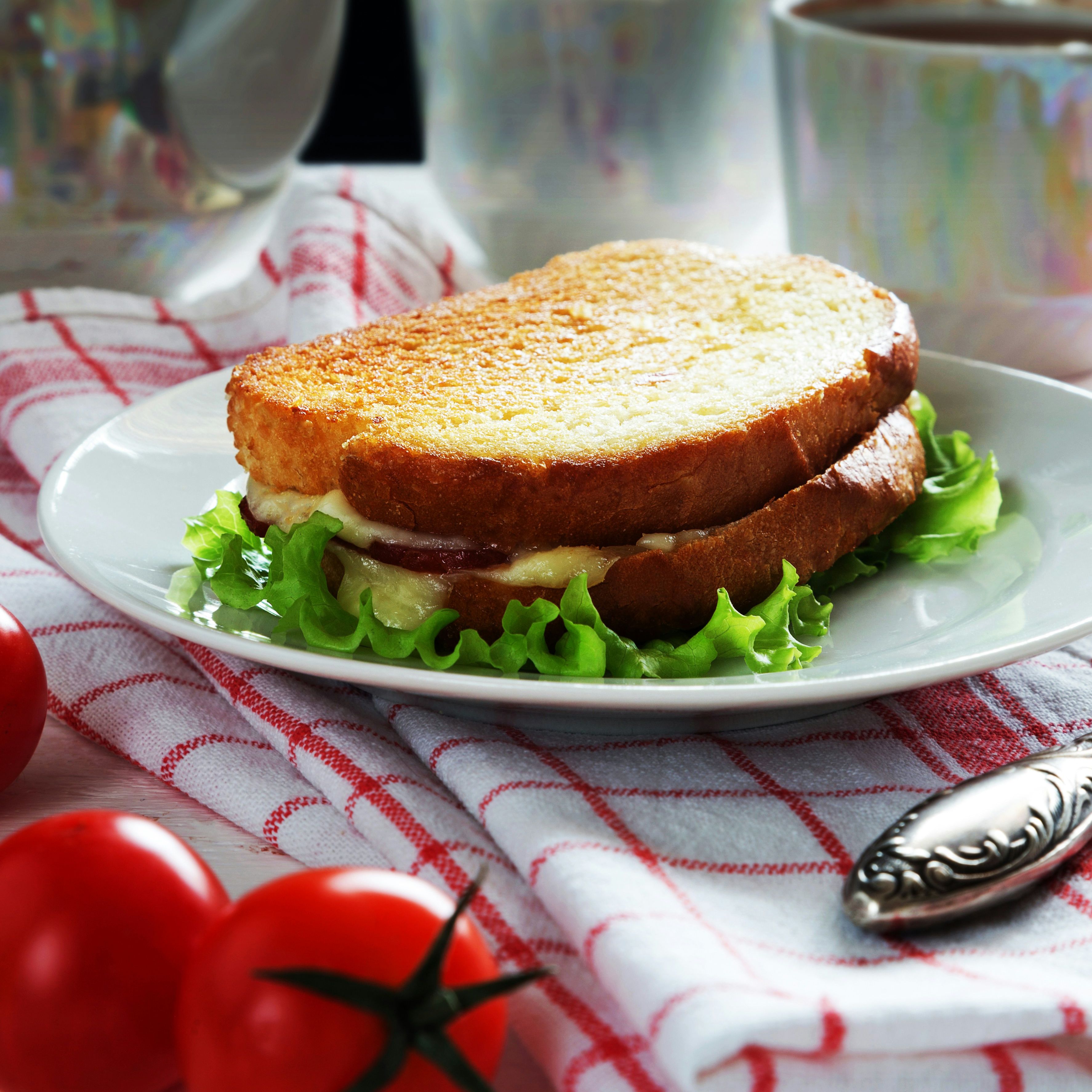 Grilled sandwich with lettuce on a white plate, next to fresh tomatoes and cups of tea.