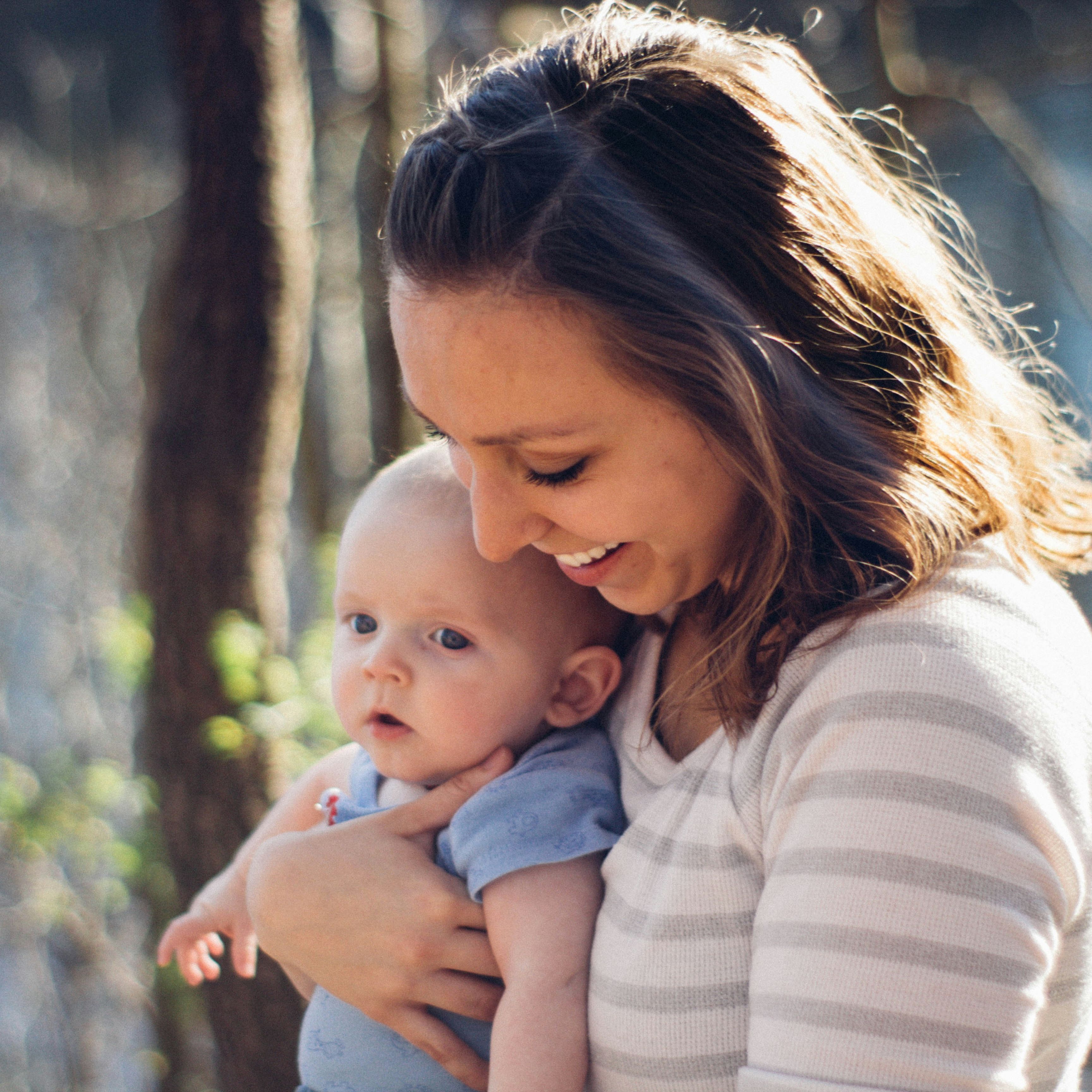 A woman holding a baby outdoors in a forest setting.