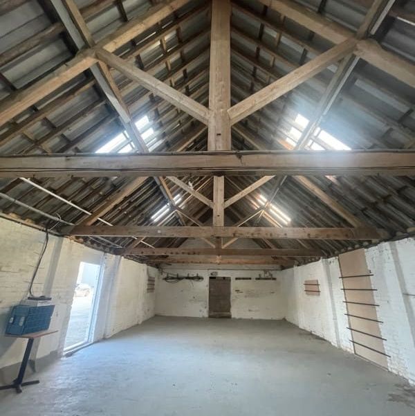 Interior of an empty barn or warehouse with exposed wooden beams and whitewashed walls.