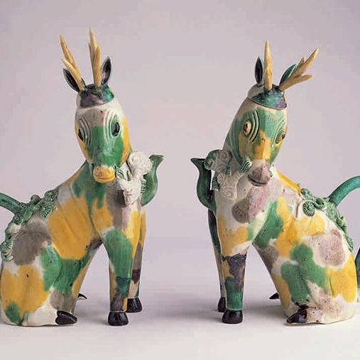Two colorful glazed ceramic figurines resembling mythical creatures with antlers and curved tails.
