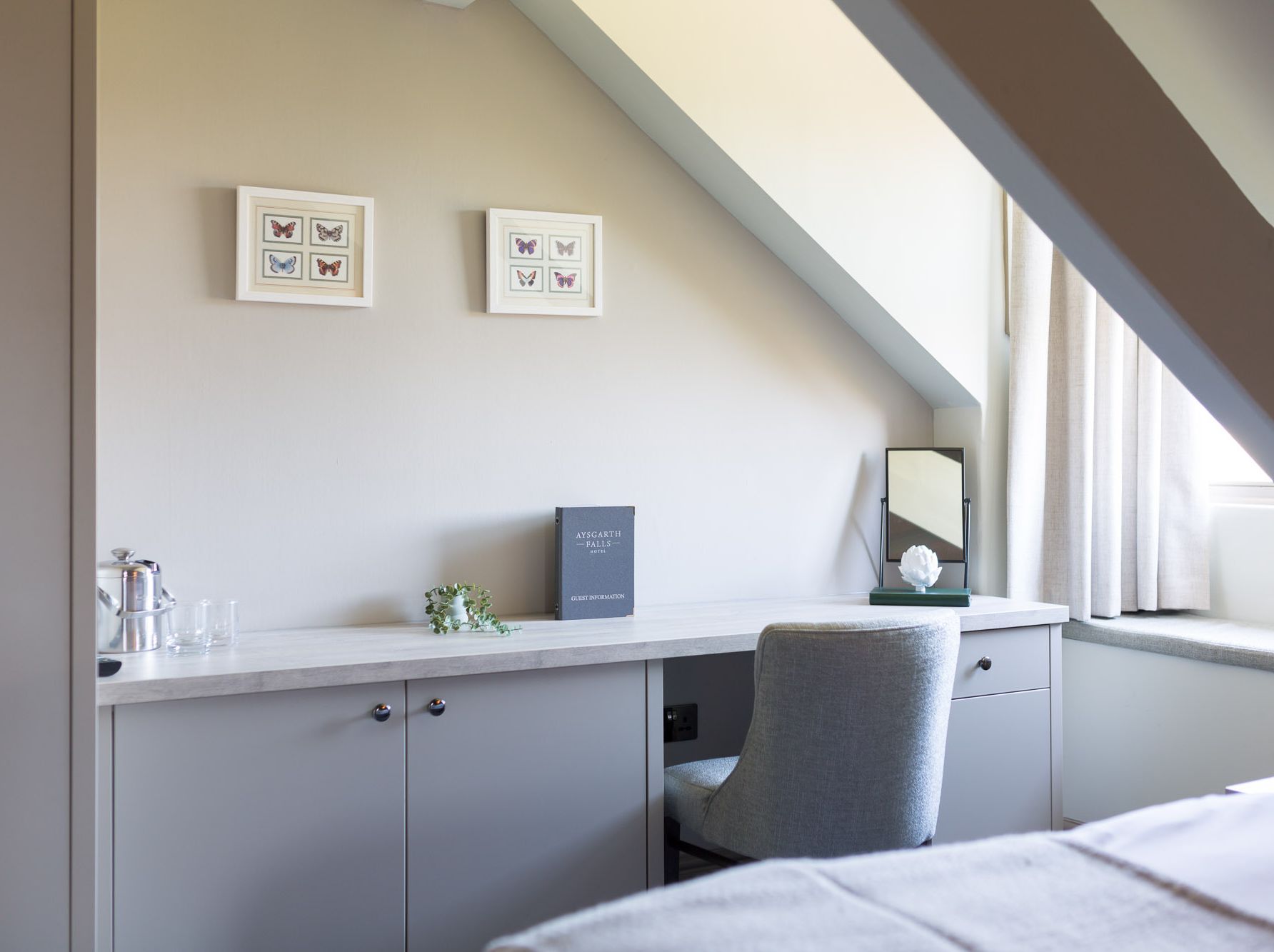 Desk area under slanted ceiling with chair, guest information book, and framed butterfly art on the wall