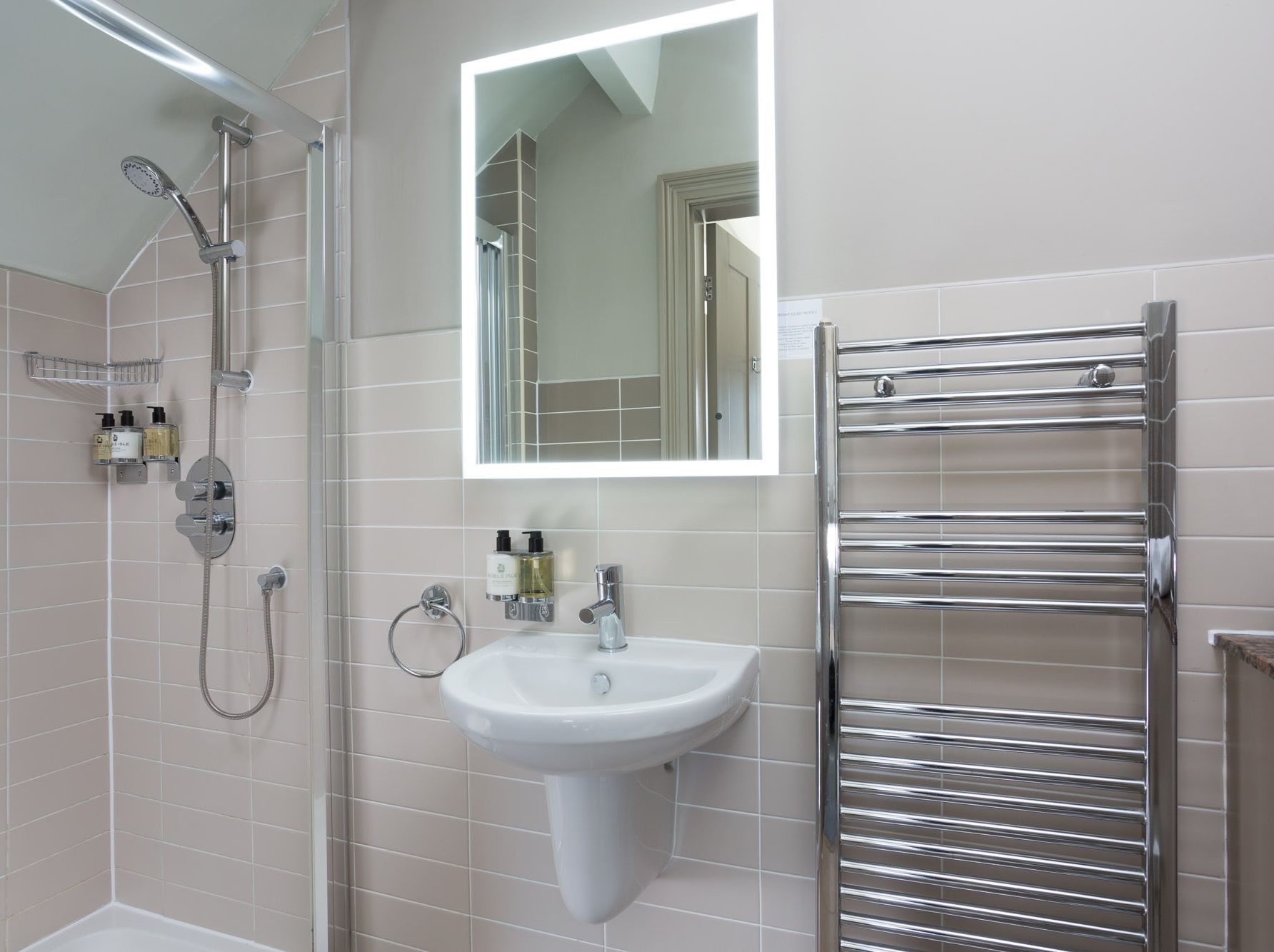 Modern bathroom with a shower, illuminated mirror, sink, and heated towel rail