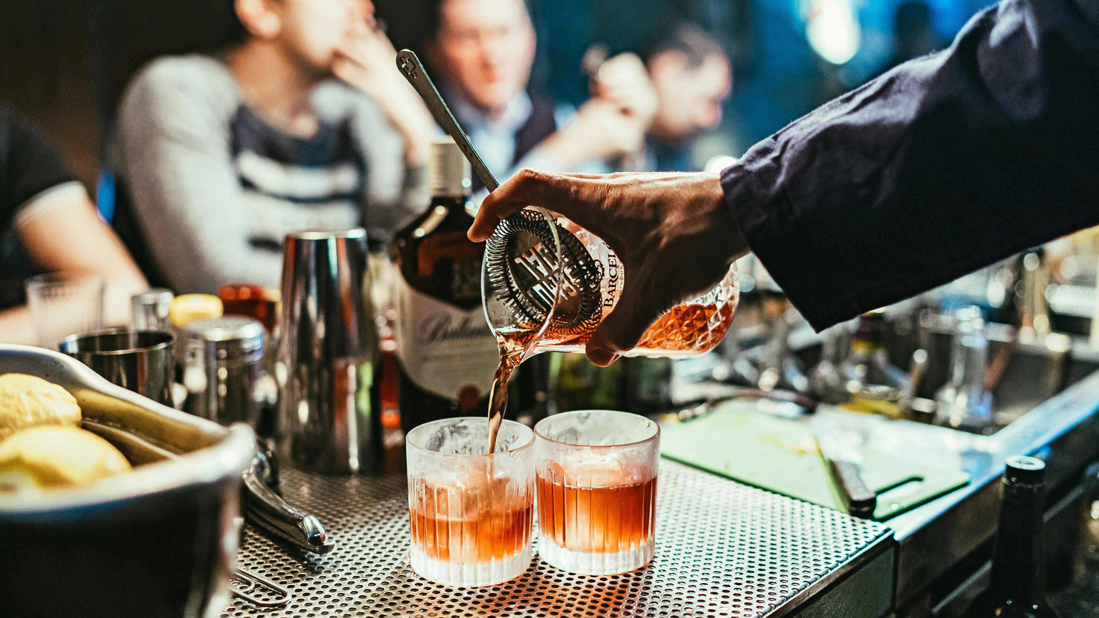Bartender pouring drinks into glasses at a busy bar with people in the background