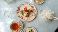 A floral-decorated tea set with a teapot, cups of tea, and a dessert with strawberries on a lace doily.