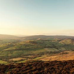 A scenic view of rolling green hills and patchwork fields under a clear blue sky
