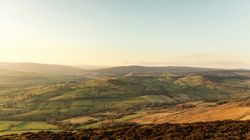 A scenic view of rolling green hills and patchwork fields under a clear blue sky