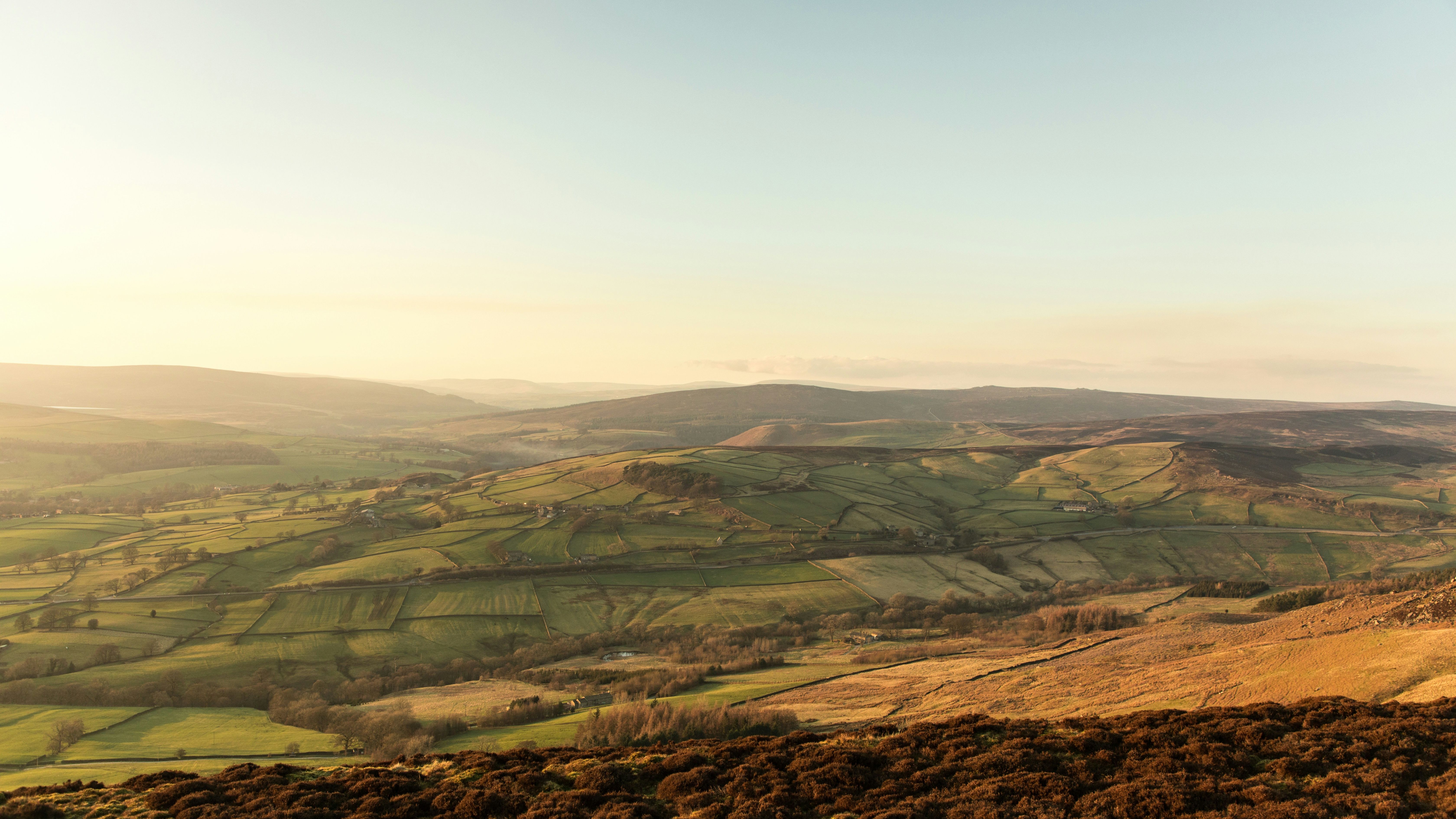 A scenic view of rolling green hills and patchwork fields under a clear blue sky