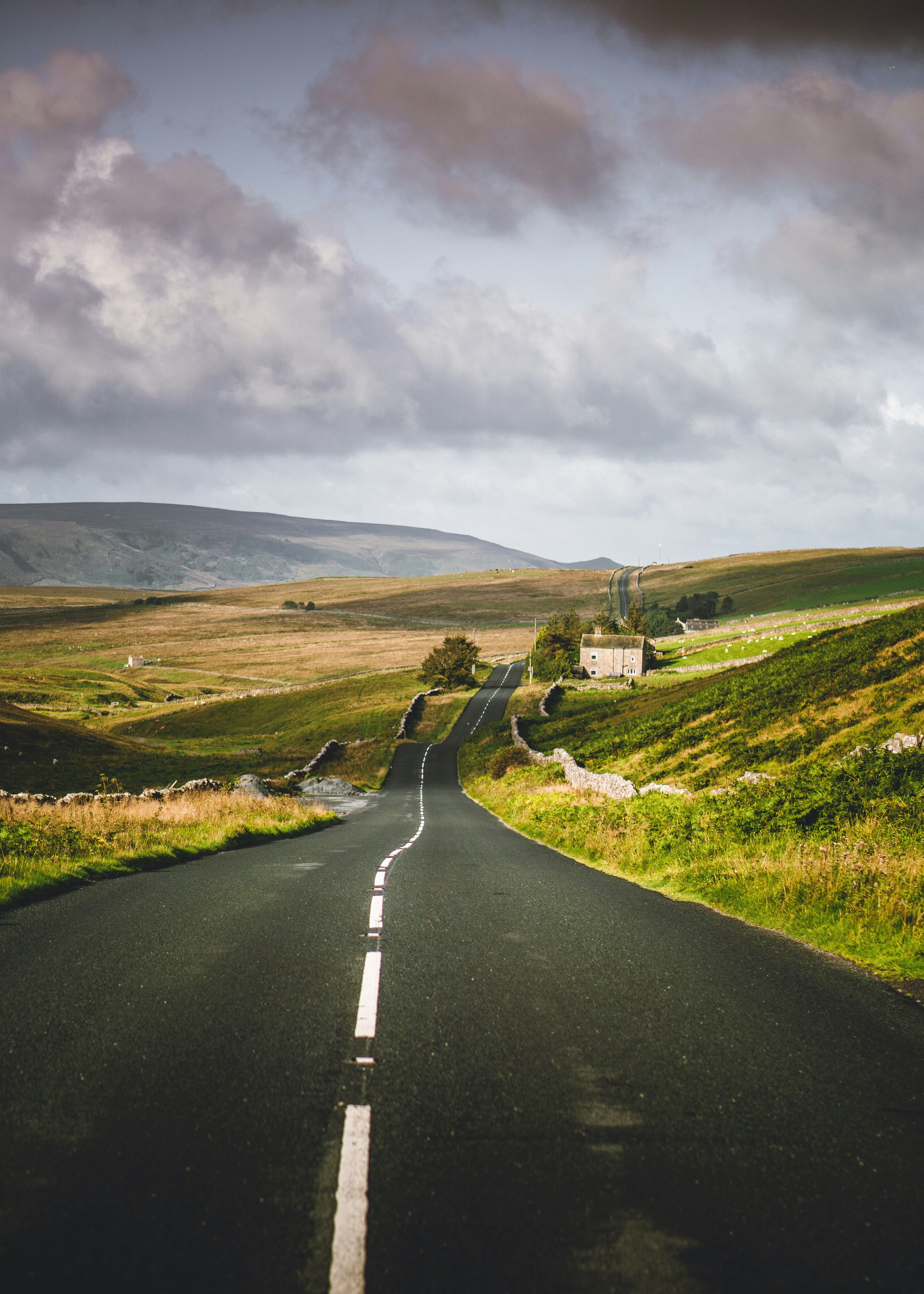 Winding country road through green hills under a cloudy sky