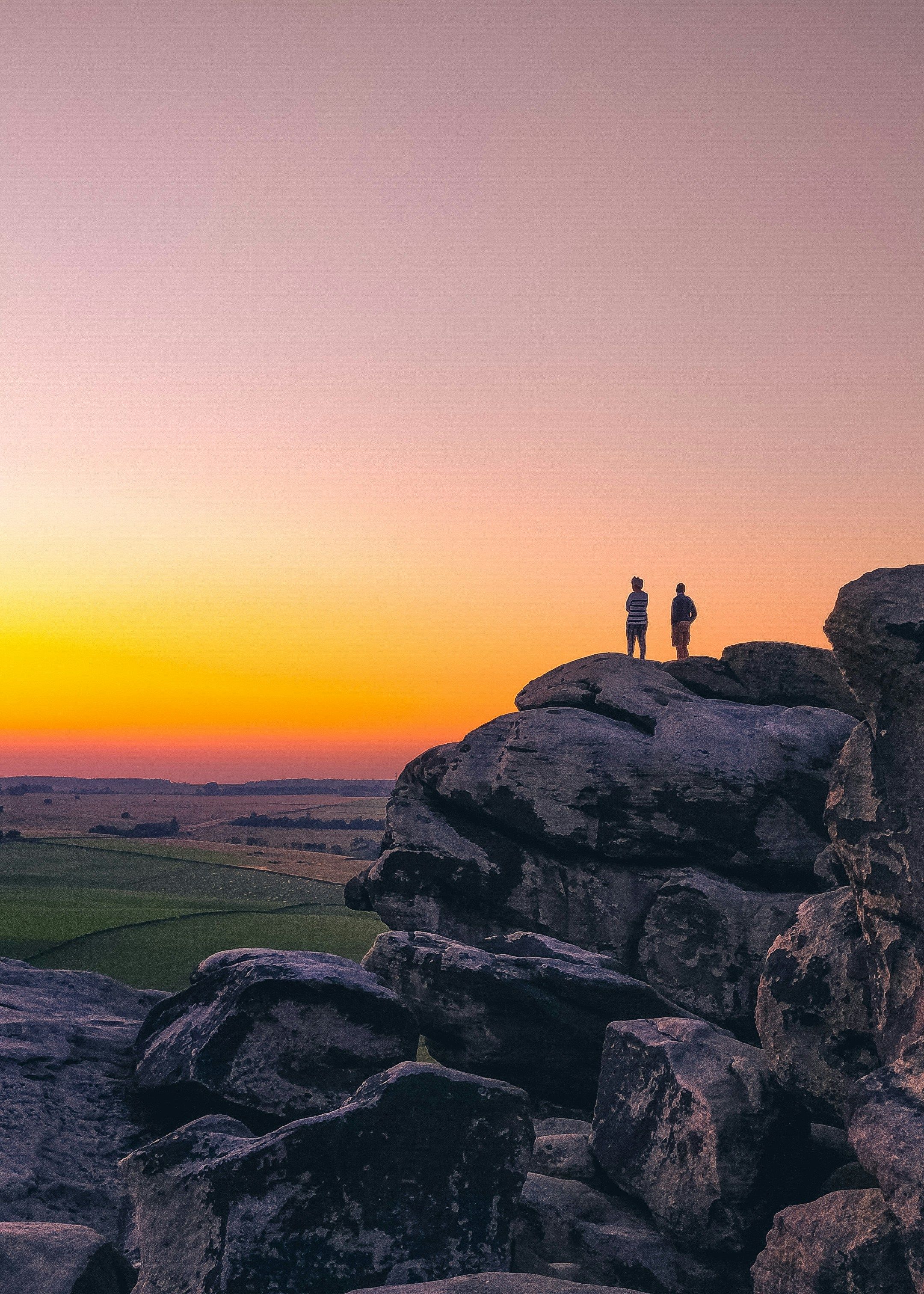 Two people standing on large rocky outcrop at sunset with colorful sky