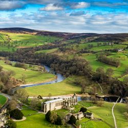 Aerial view of green countryside with a winding river and an old stone building with ruins.