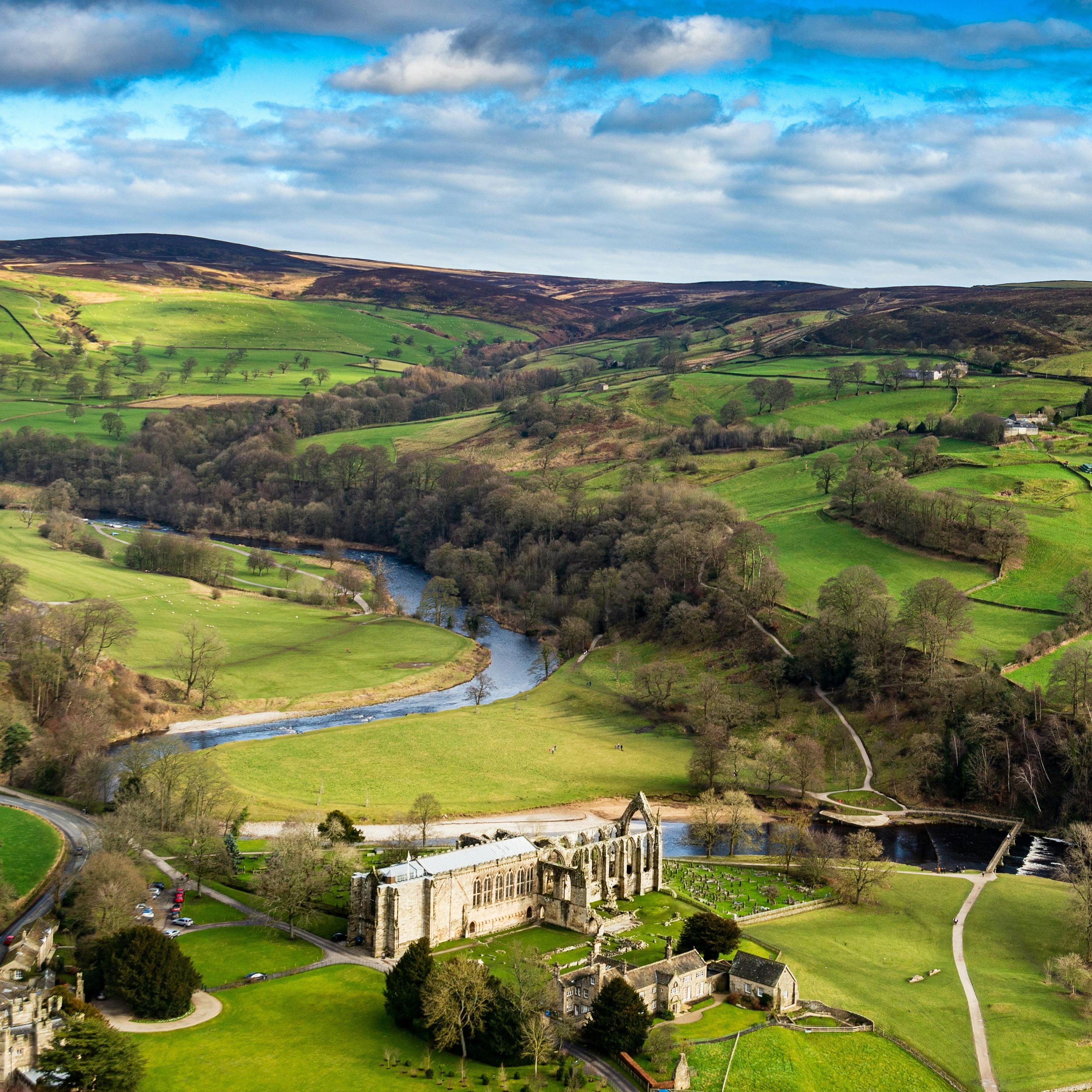 Aerial view of green countryside with a winding river and an old stone building with ruins.