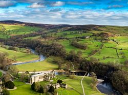 Aerial view of green countryside with a winding river and an old stone building with ruins.