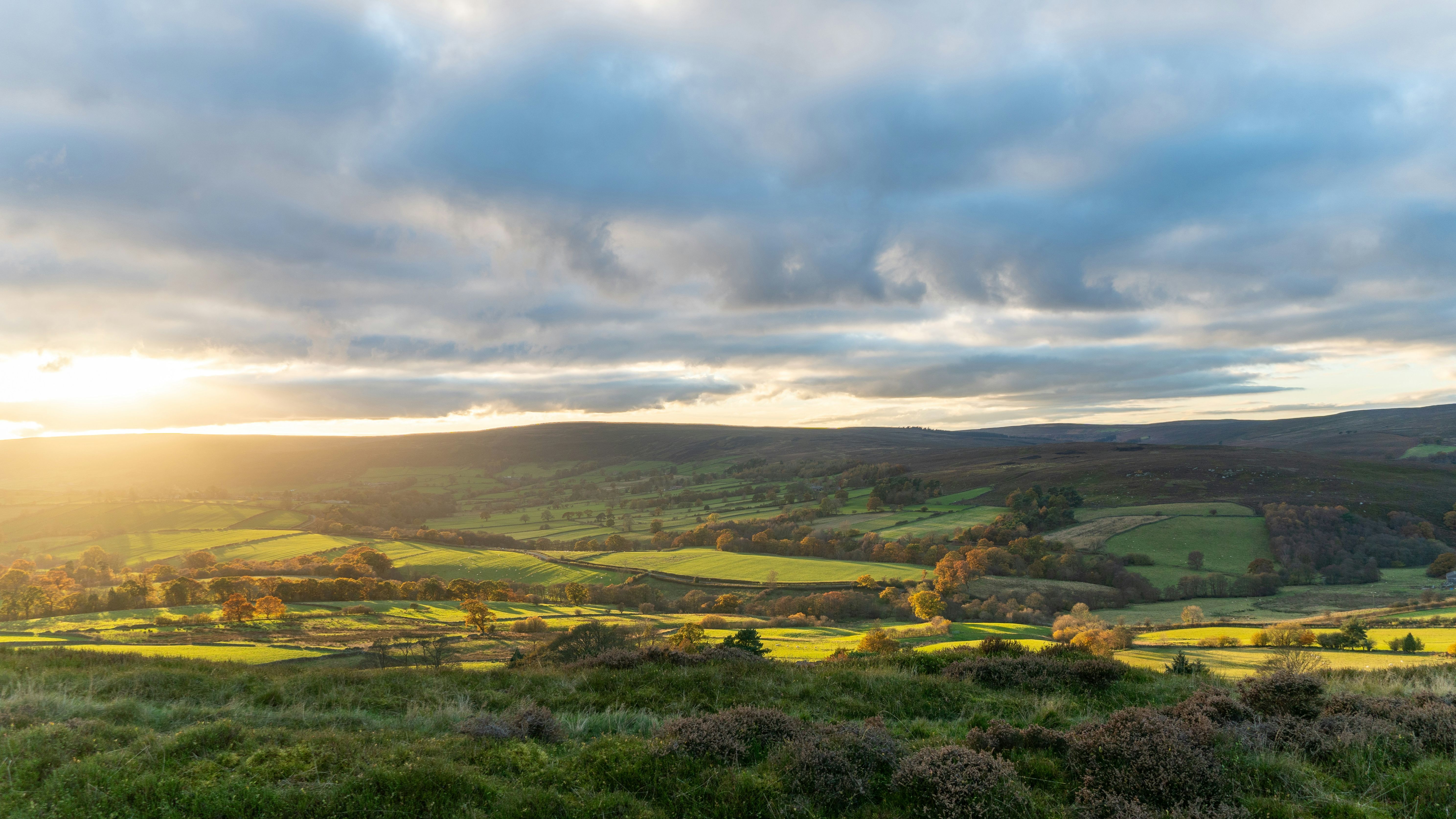 View of rolling green countryside hills with the sun setting behind clouds
