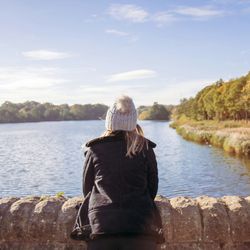 Person wearing a coat and knit hat looking out over a river with trees along the banks.