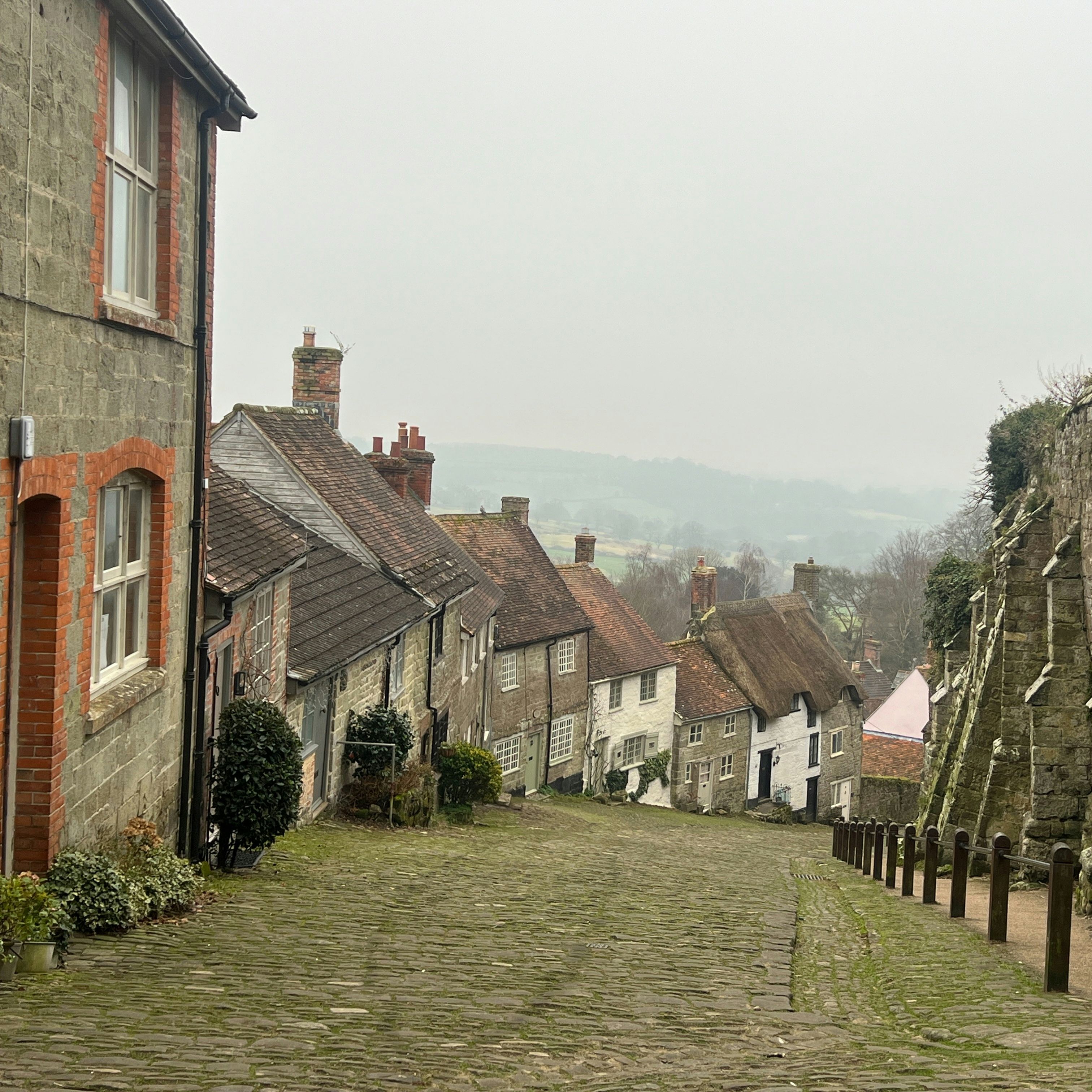 A steep cobblestone street lined with old stone houses and a stone wall in a picturesque English village.