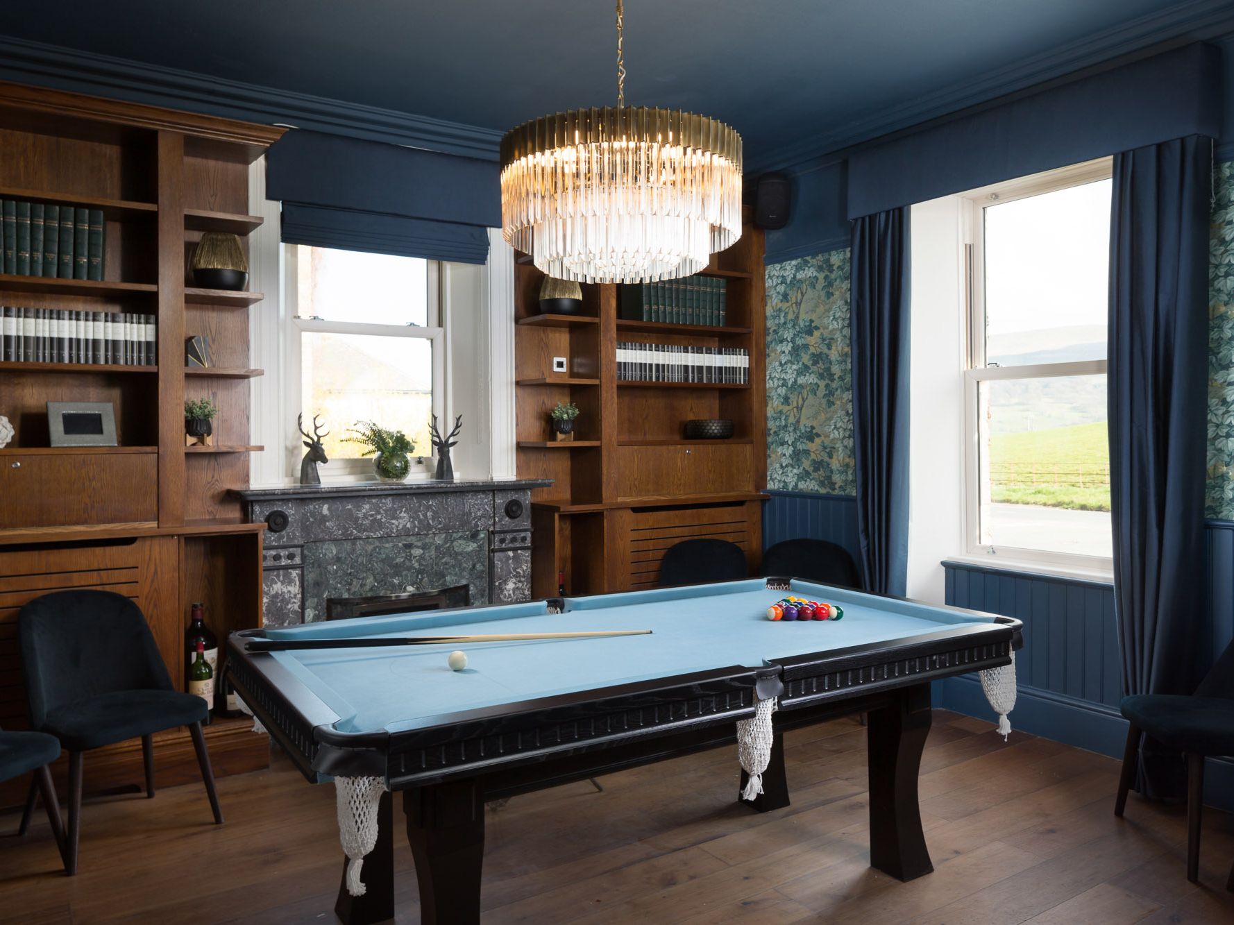 Elegant billiards room with blue pool table, chandelier, and large windows