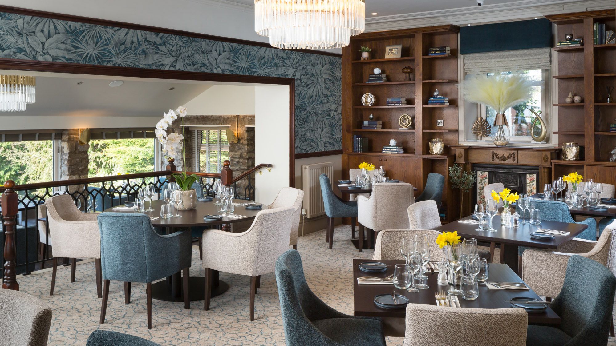 Elegant hotel dining room with blue and cream chairs, set tables, and bookshelves.