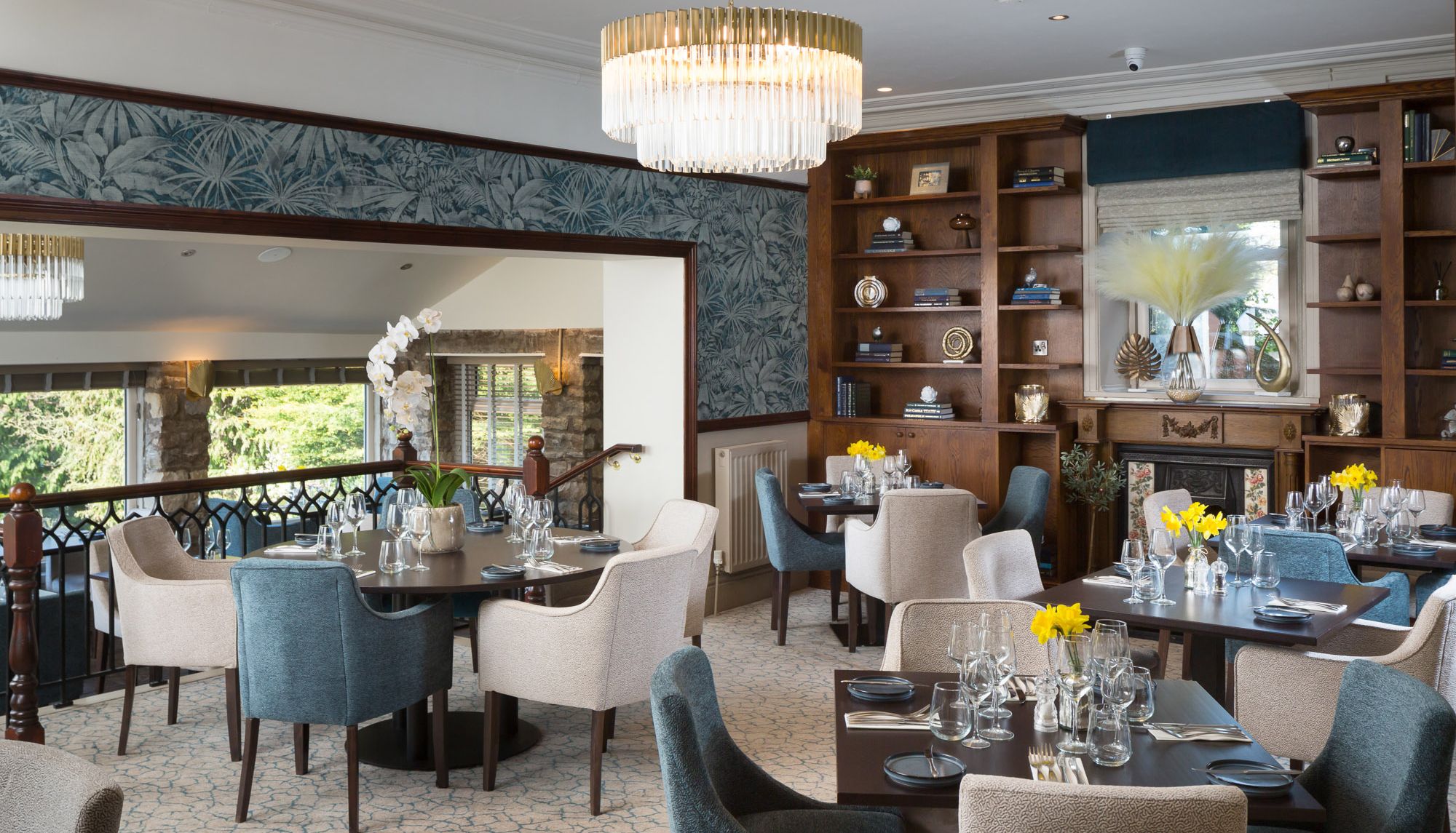 Elegant hotel dining room with blue and cream chairs, set tables, and bookshelves.