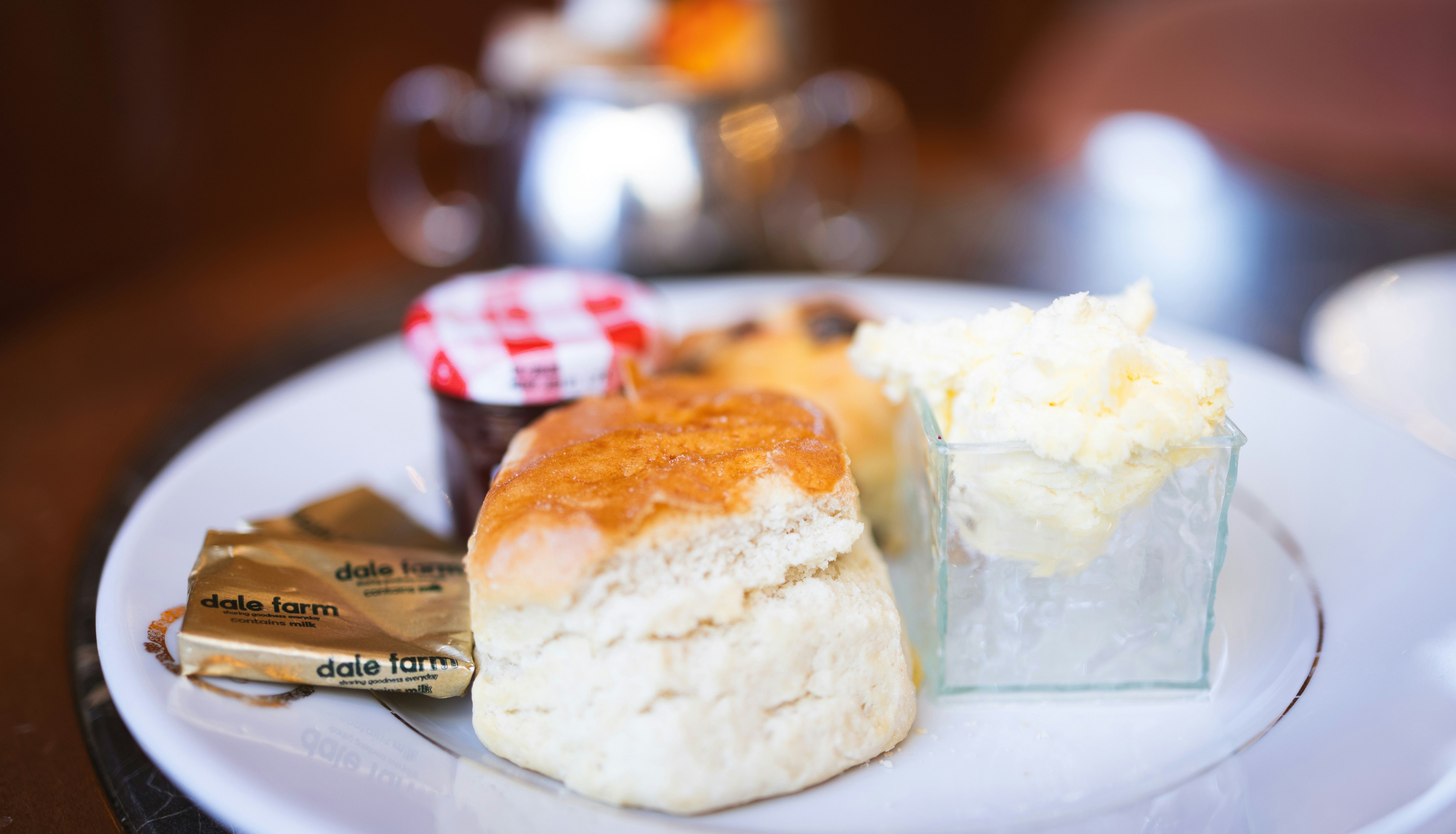A plate with a scone, clotted cream, butter packets, and a small jar of strawberry jam