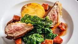Gourmet plated dish featuring slices of roasted meat, greens, potatoes, and sauce on a white plate