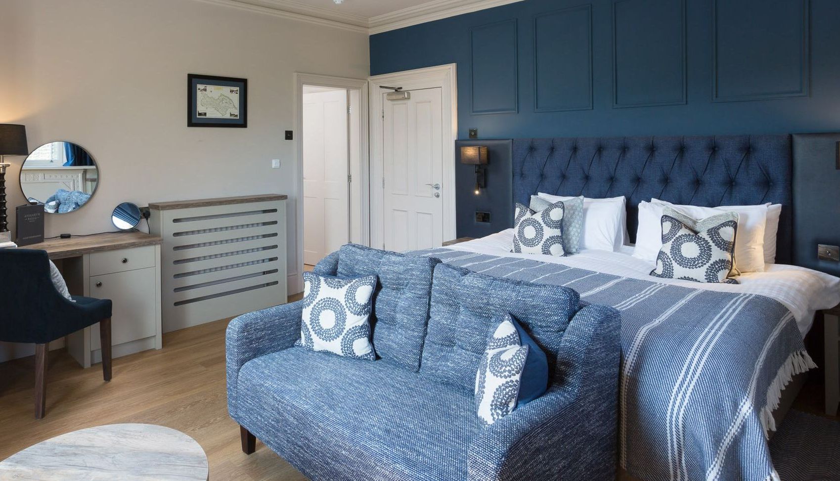 Modern hotel room with blue and white decor, a large bed, blue sofa, and work desk