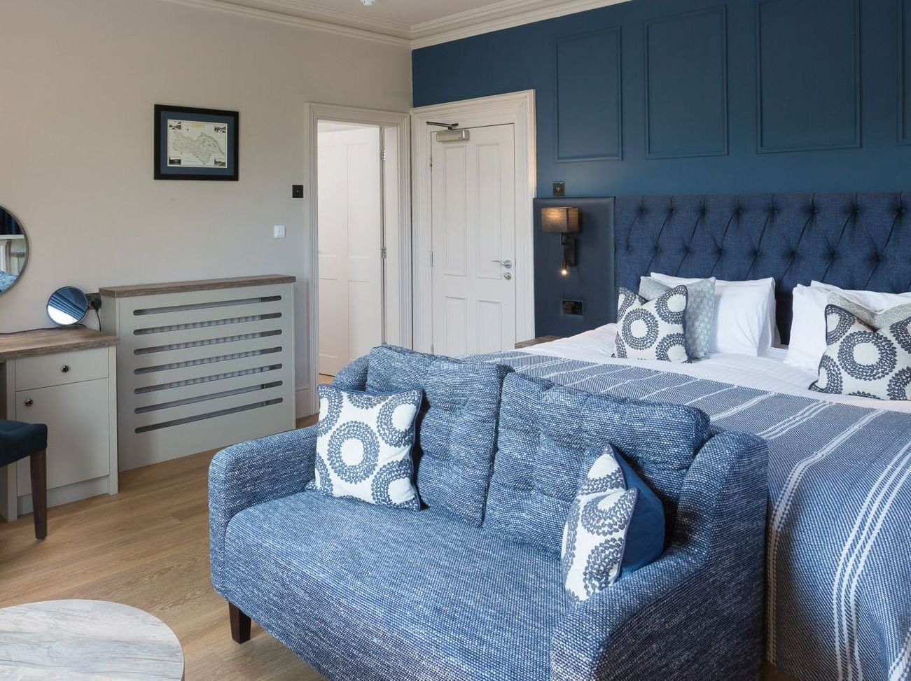 Modern hotel room with blue and white decor, a large bed, blue sofa, and work desk