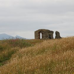 Ruins of an old stone building in a grassy field with mountains in the background
