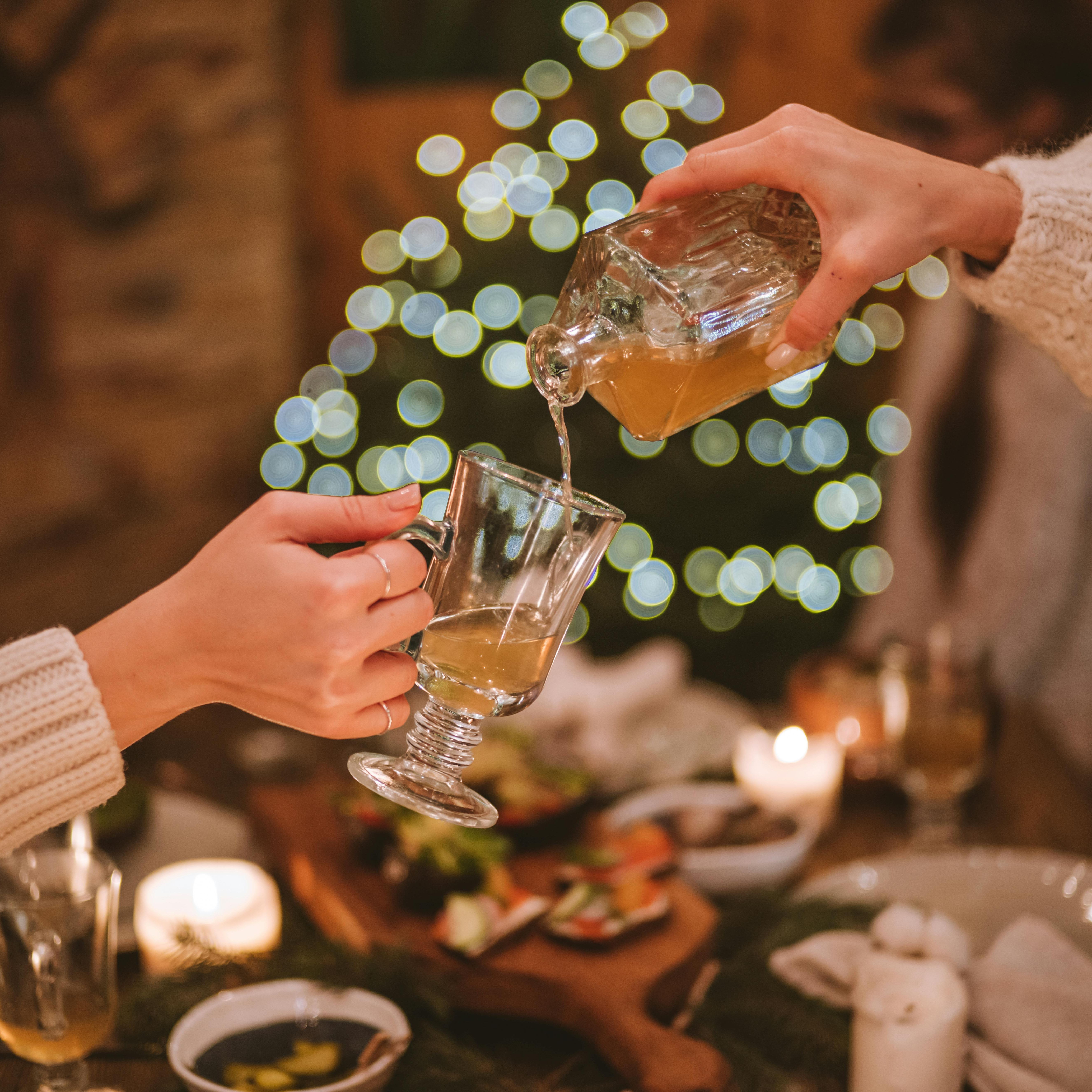 Two people pouring a drink into a glass at a cozy, festive dinner table