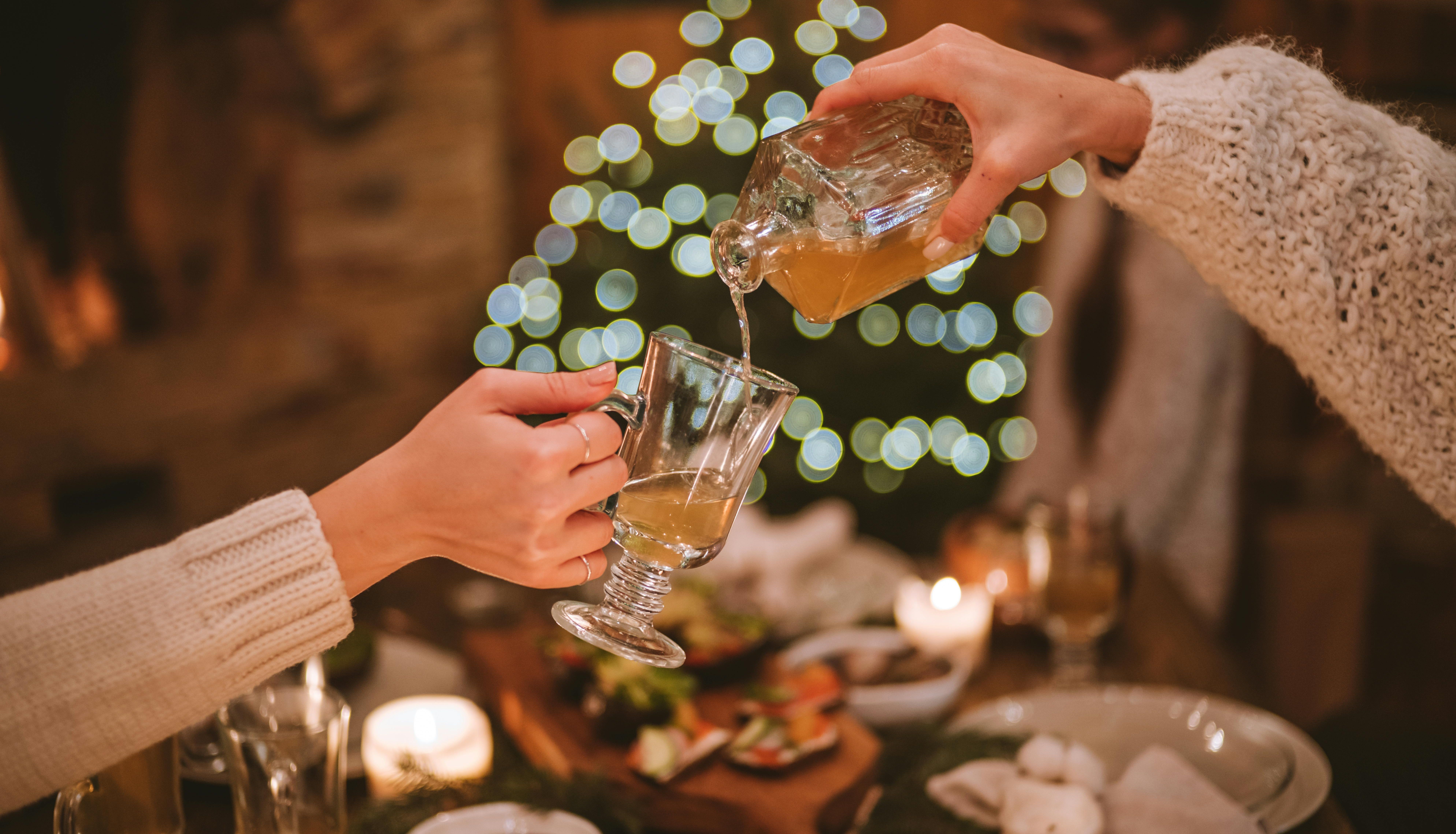 Two people pouring a drink into a glass at a cozy, festive dinner table