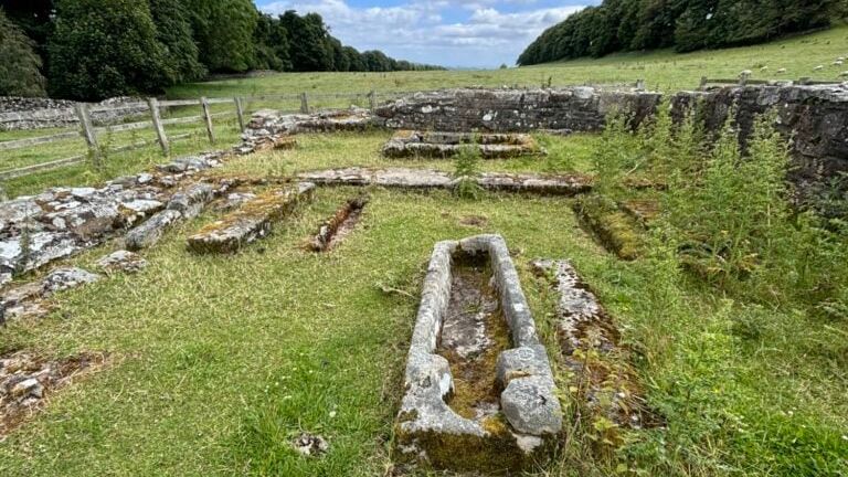 Ruins of Penhill Preceptory with old stone structures and a sarcophagus on grassy land.