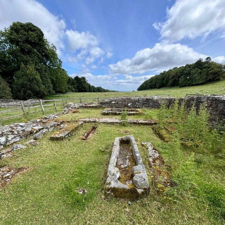 Ruins of Penhill Preceptory with old stone structures and a sarcophagus on grassy land.