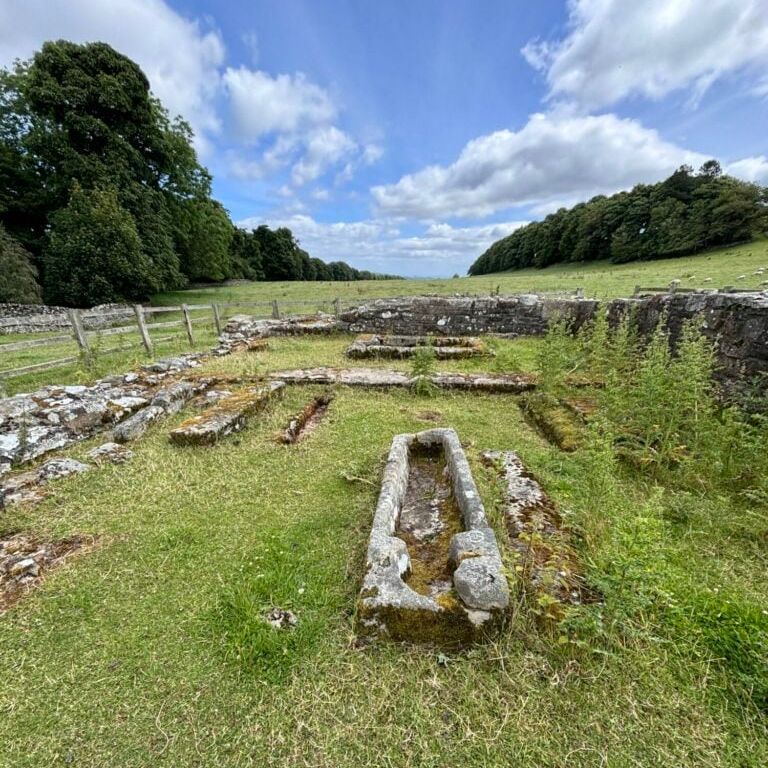 Ruins of Penhill Preceptory with old stone structures and a sarcophagus on grassy land.