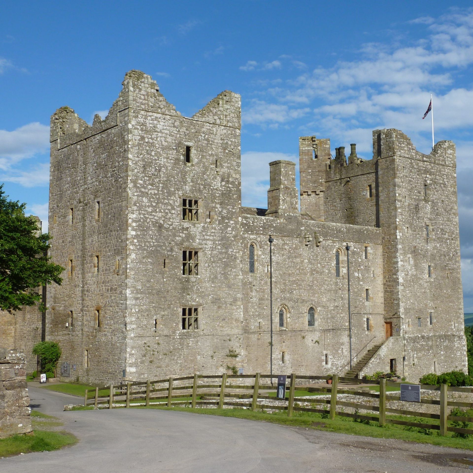 Stone medieval Bolton Castle with towers and a flag, set against a blue sky and green countryside.