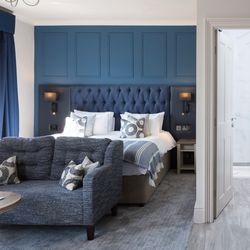 Modern hotel room with blue accents, visible bed, sofa, freestanding bathtub, and a bathroom entrance.