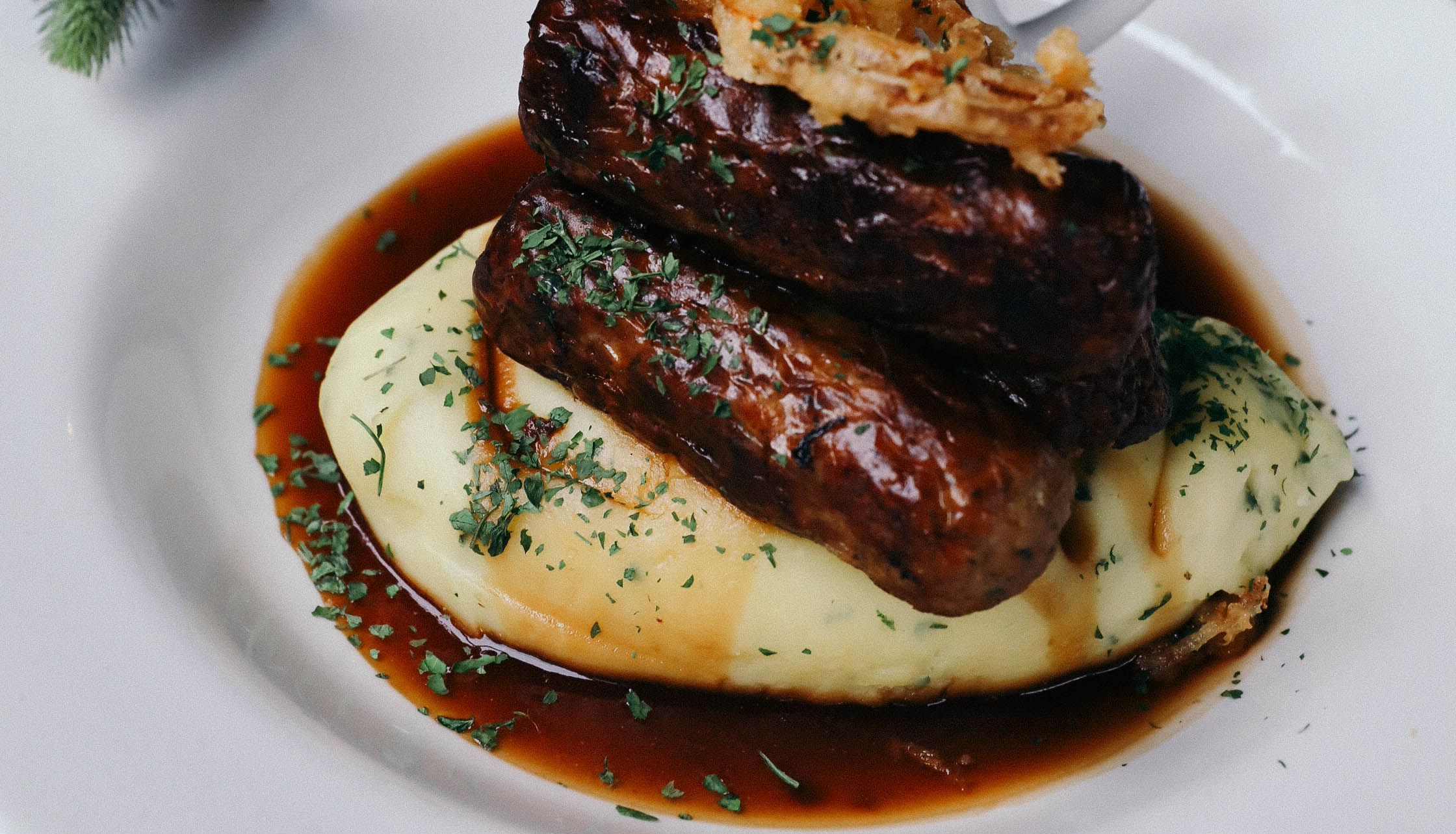 Bangers and mash with gravy, onion rings, and herbs served on a white plate
