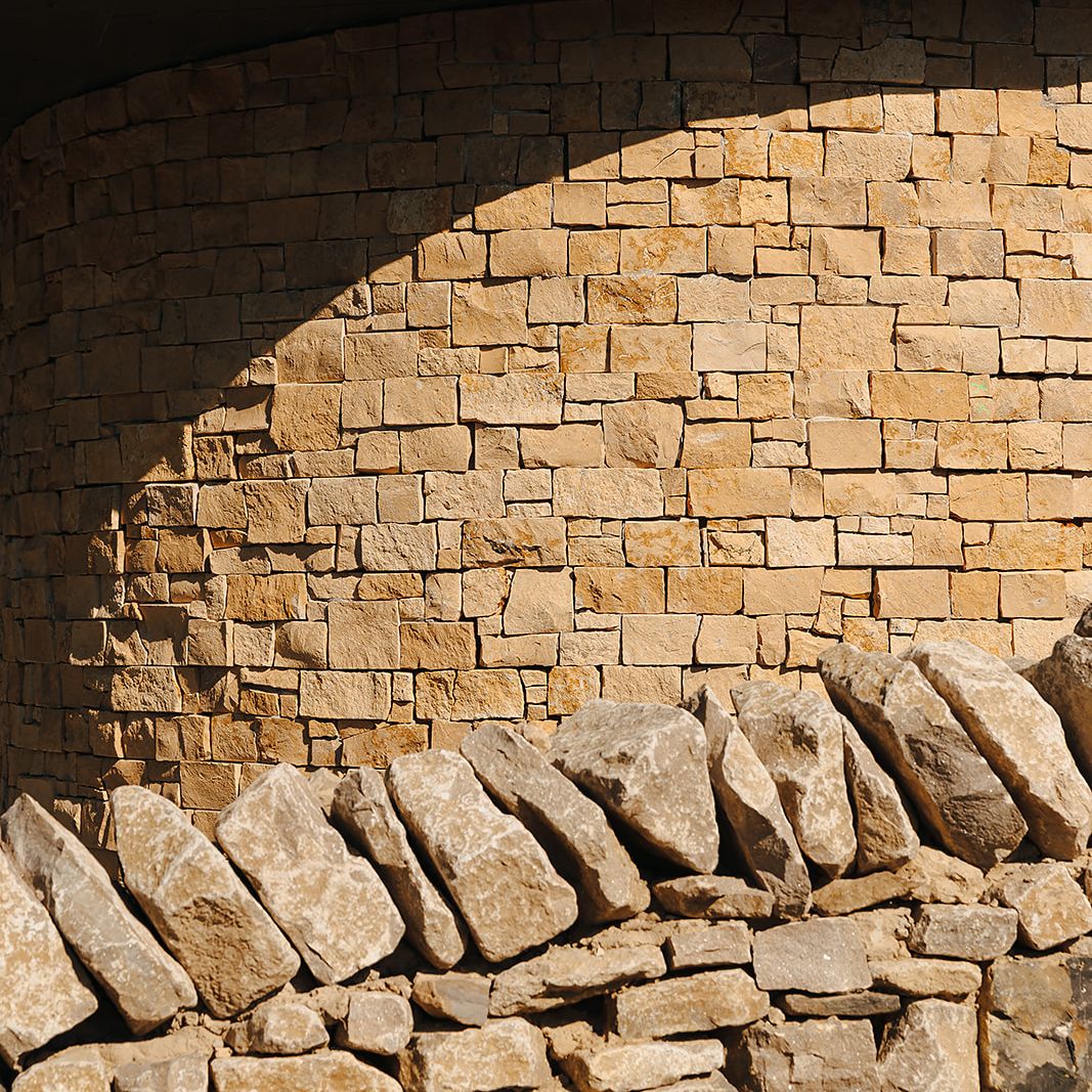 Close-up of a curved stone wall with a row of larger stones at the base and a metal roof above