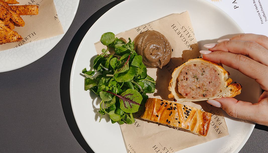 A selection of appetizers including a bowl of mixed olives, a glass of rosé wine, and a plate with a sausage roll, greens, and pâté.