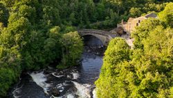 Stone bridge over a river surrounded by trees and a countryside house