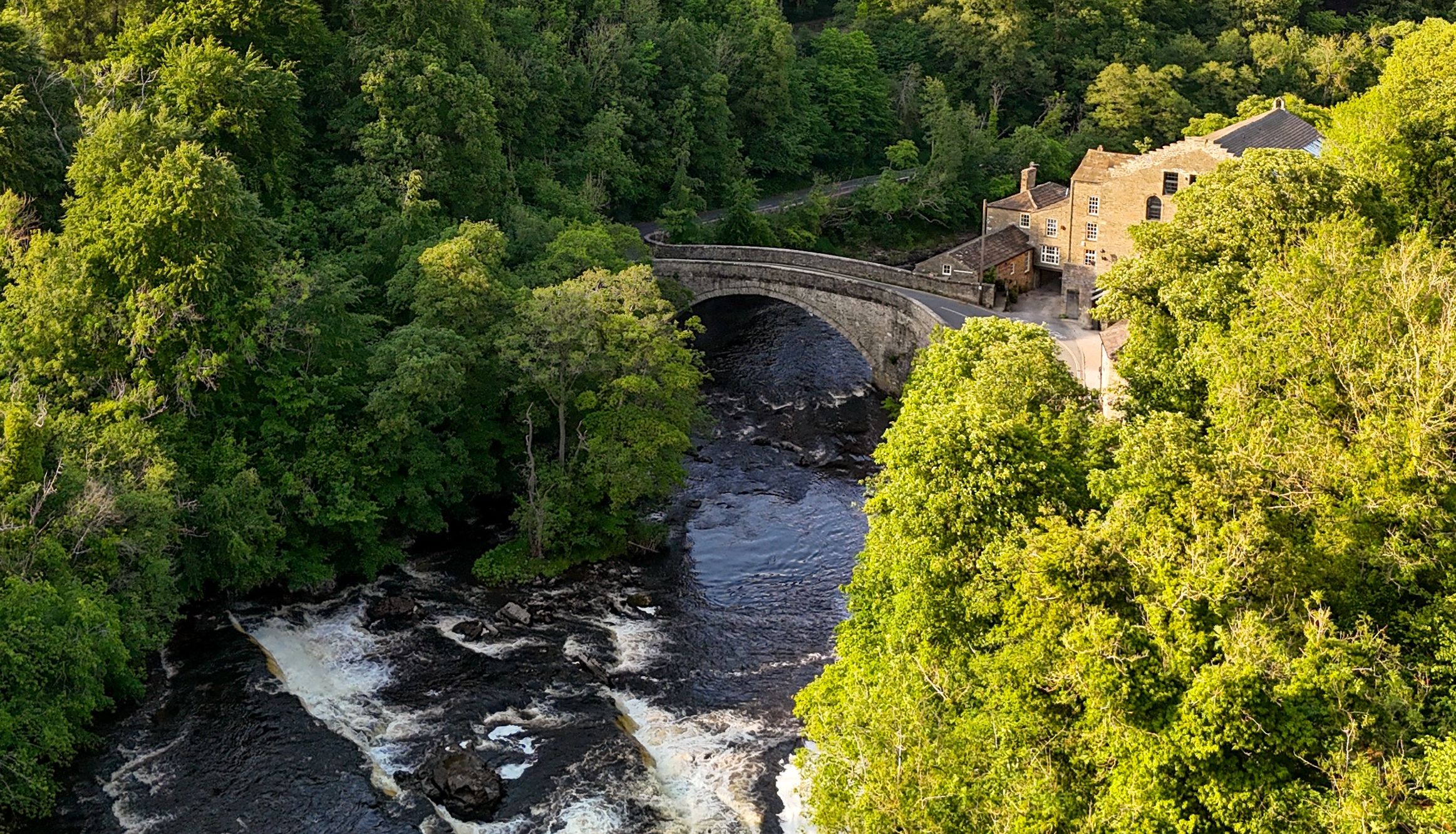 Stone bridge over a river surrounded by trees and a countryside house