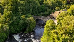 Stone bridge over a river surrounded by trees and a countryside house