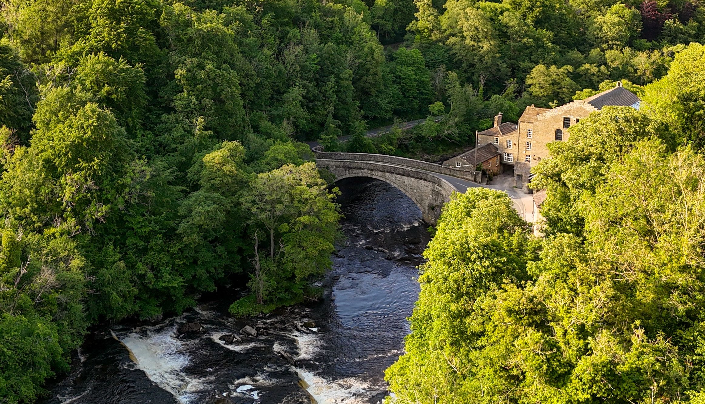 Stone bridge over a river surrounded by trees and a countryside house