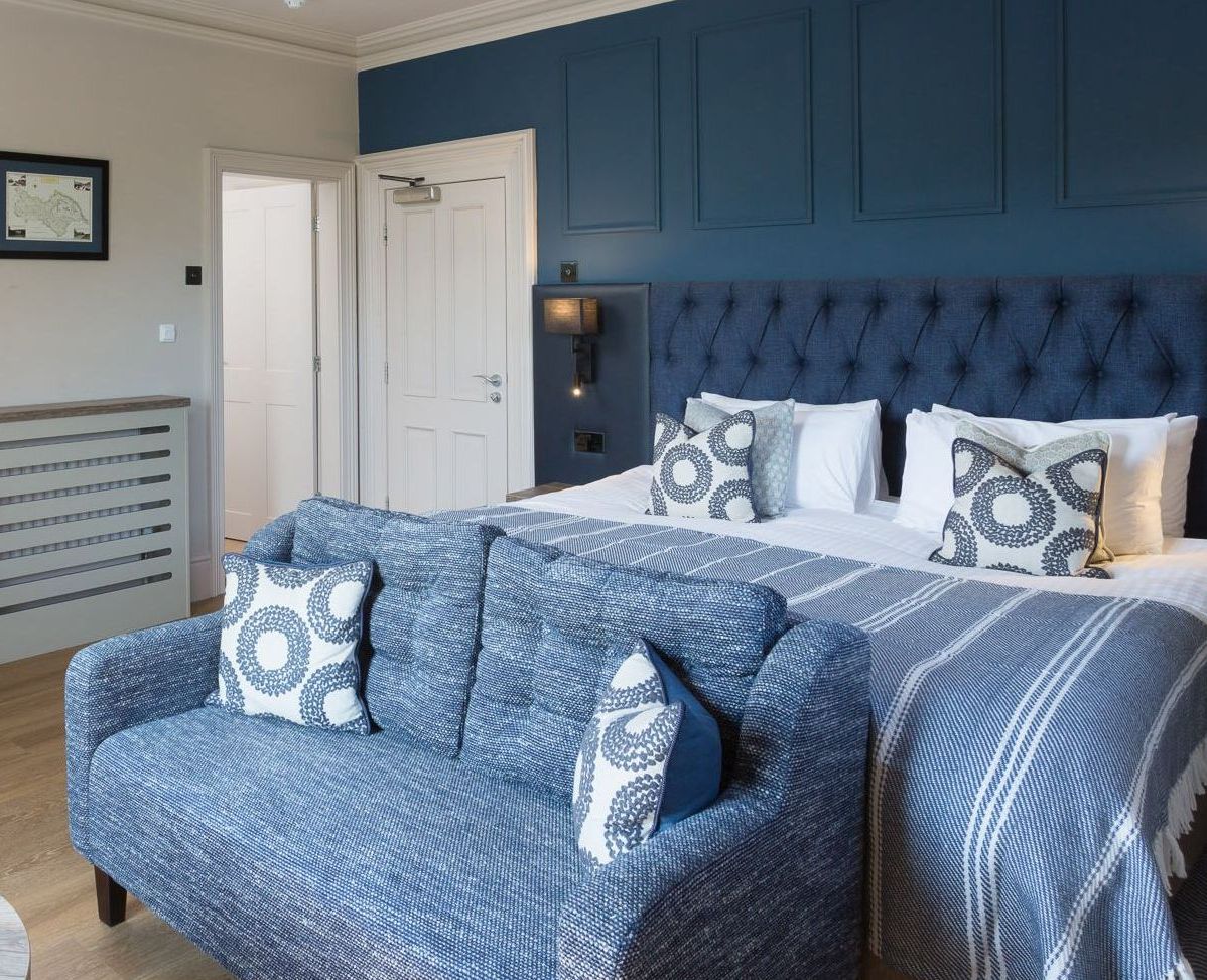 Modern hotel room with king-sized bed, blue sofa, writing desk, and stylish decor