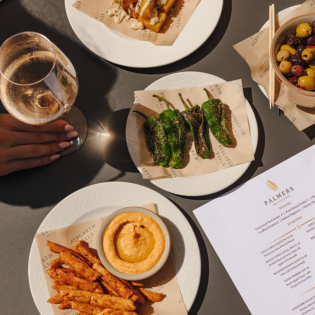 A selection of tapas-style dishes and a glass of wine on an outdoor table at Aysgarth Falls Hotel.