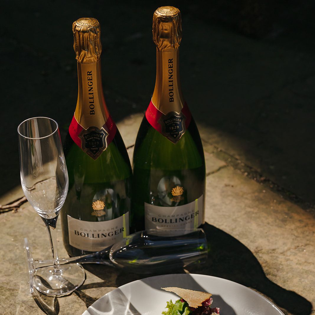 Two bottles of Bollinger champagne, two champagne flutes, and a gourmet appetizer on a white plate.