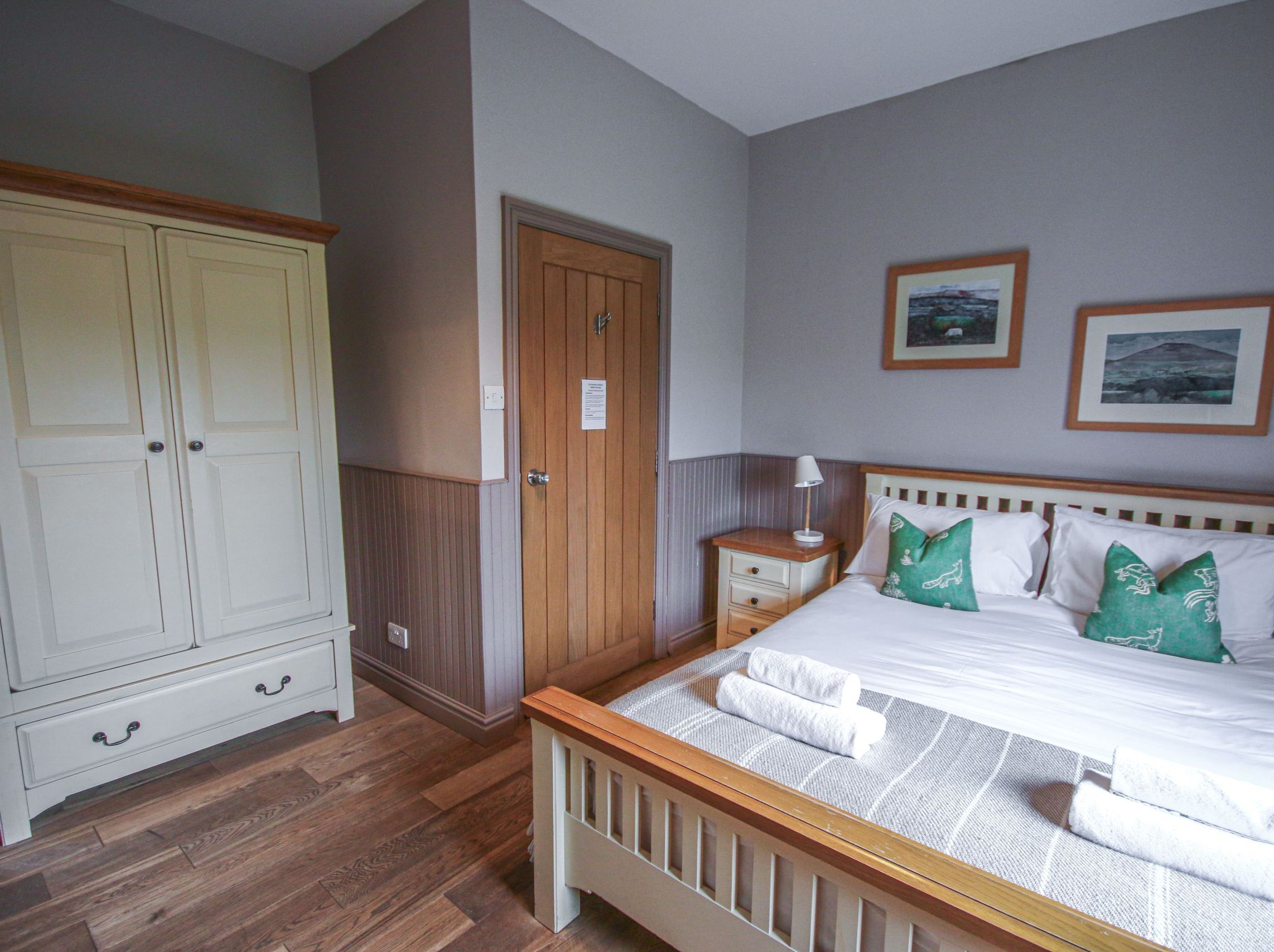 Cozy bedroom with a double bed, green pillows, white wardrobe, and wooden flooring.
