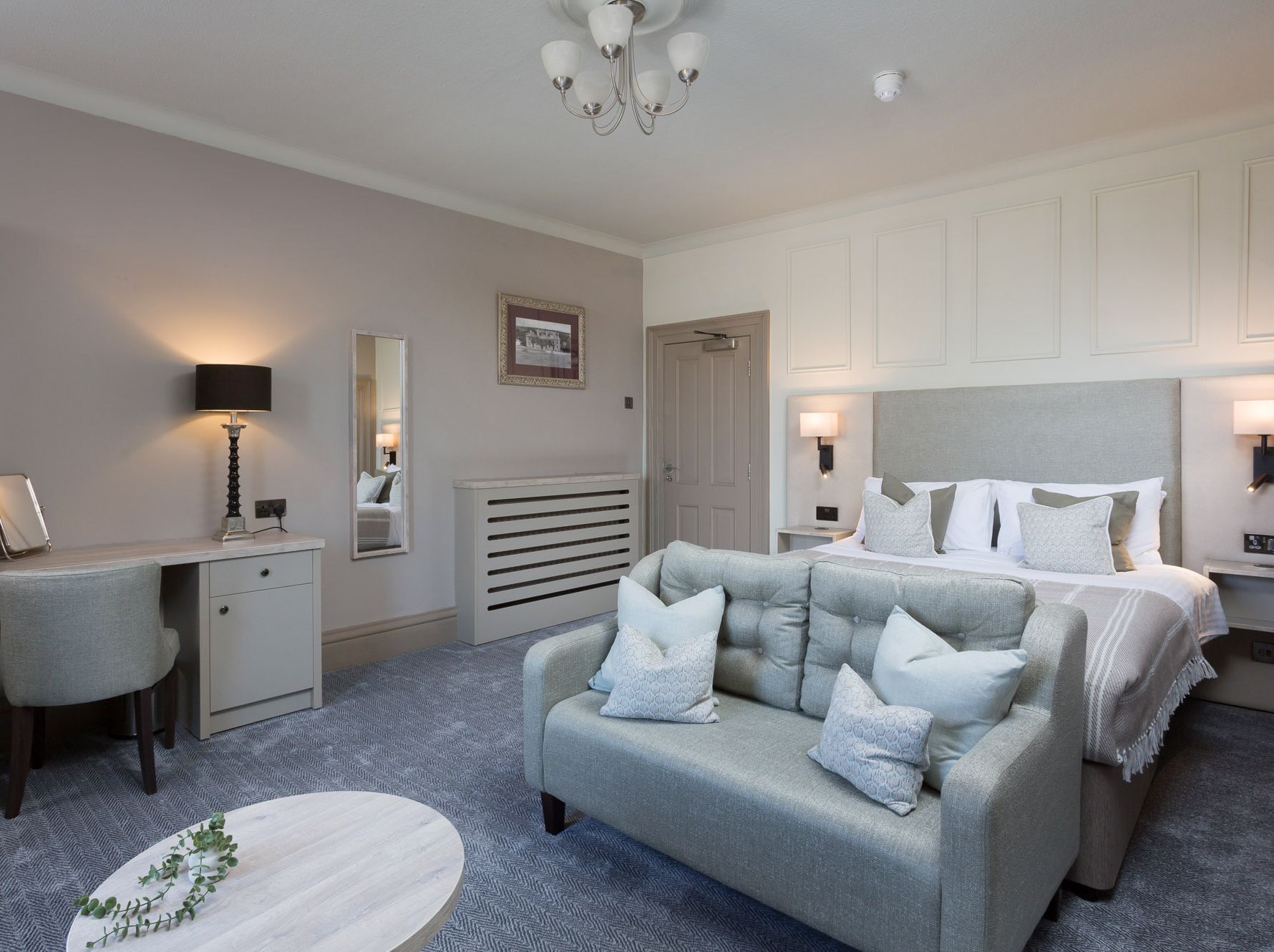 Modern hotel room with a bed, sofa, desk, and neutral decor