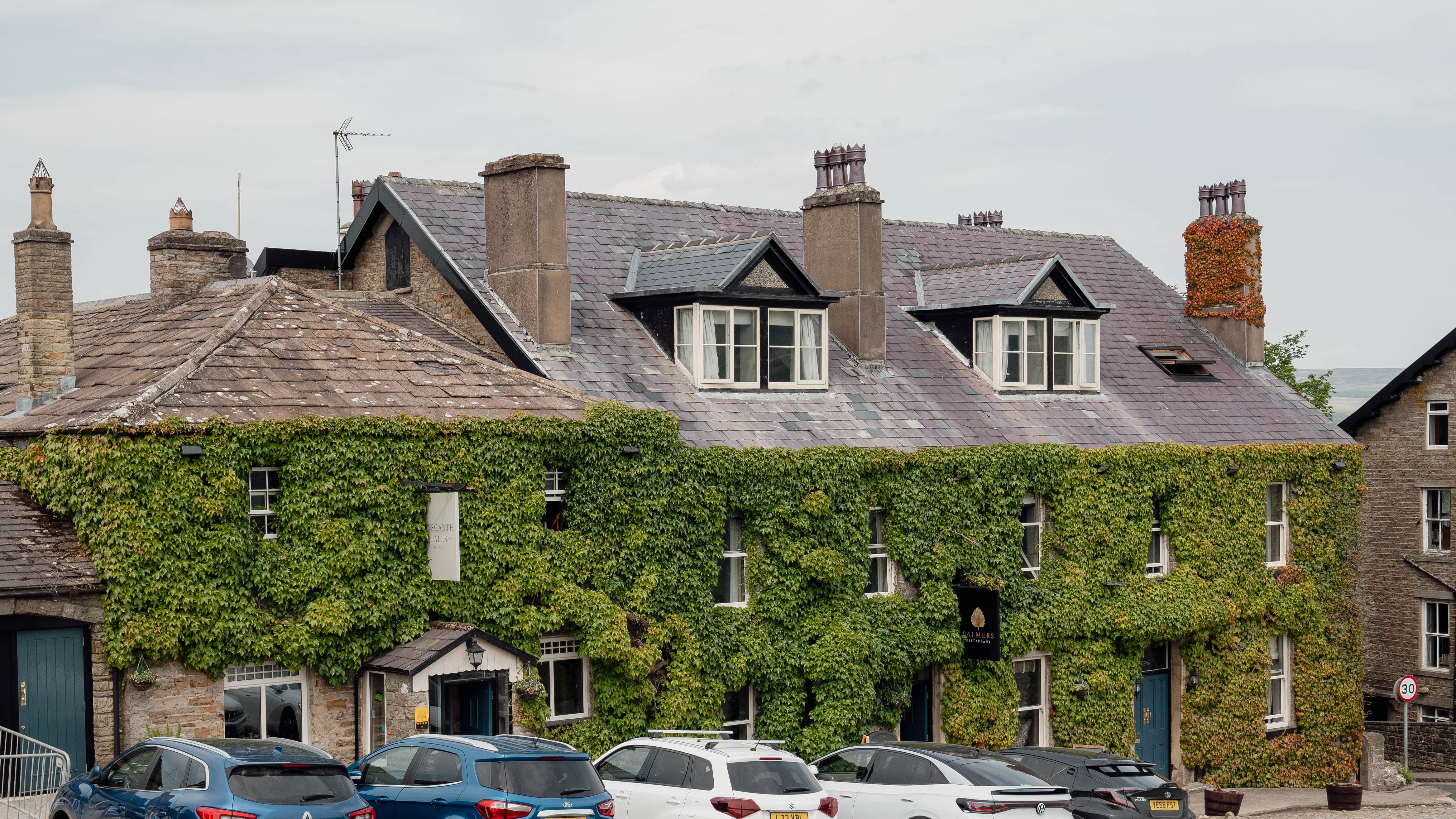 Stone building covered in green ivy with several parked cars in front