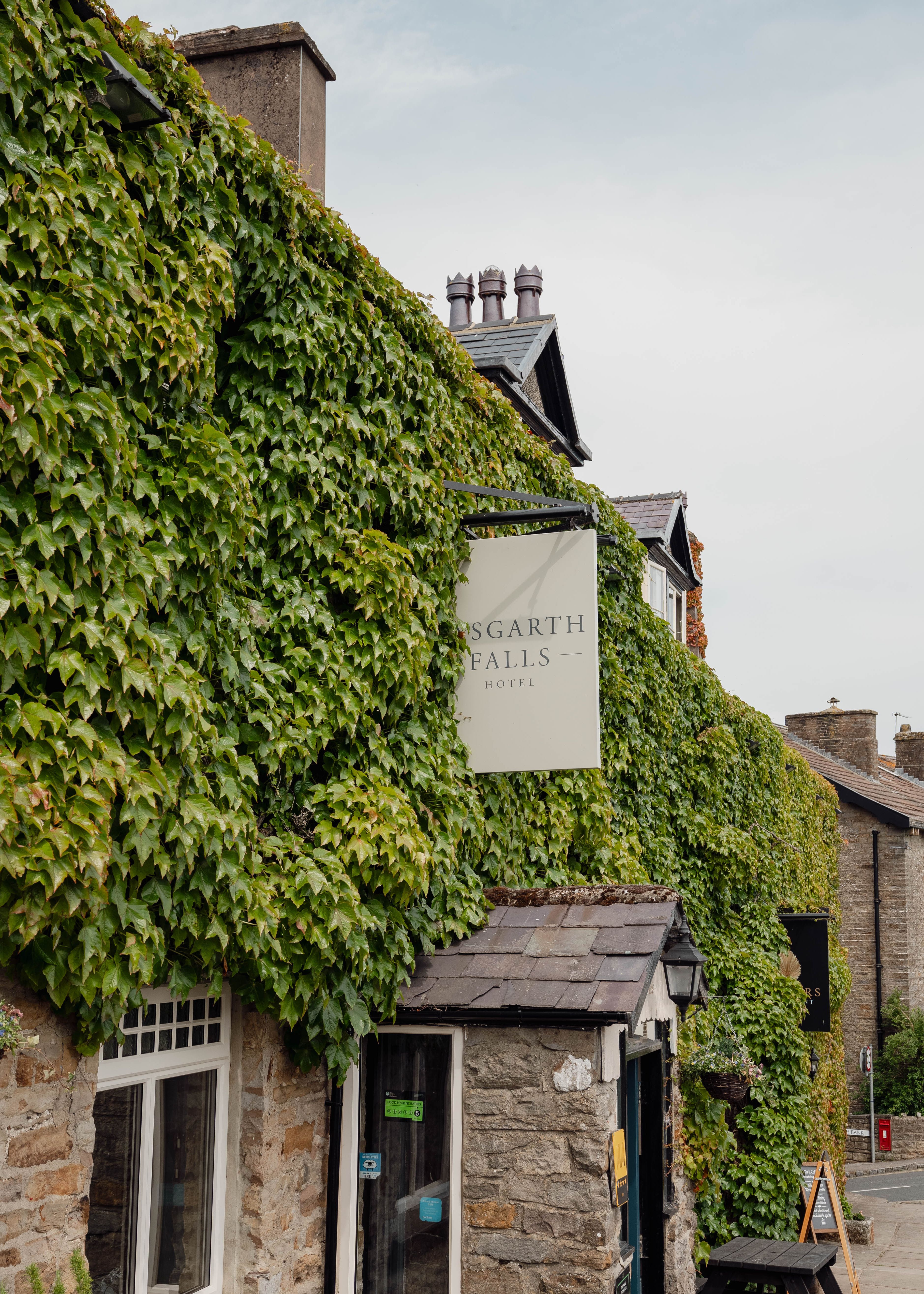 Stone building covered in thick green ivy with a sign reading 'Aysgarth Falls Hotel.'