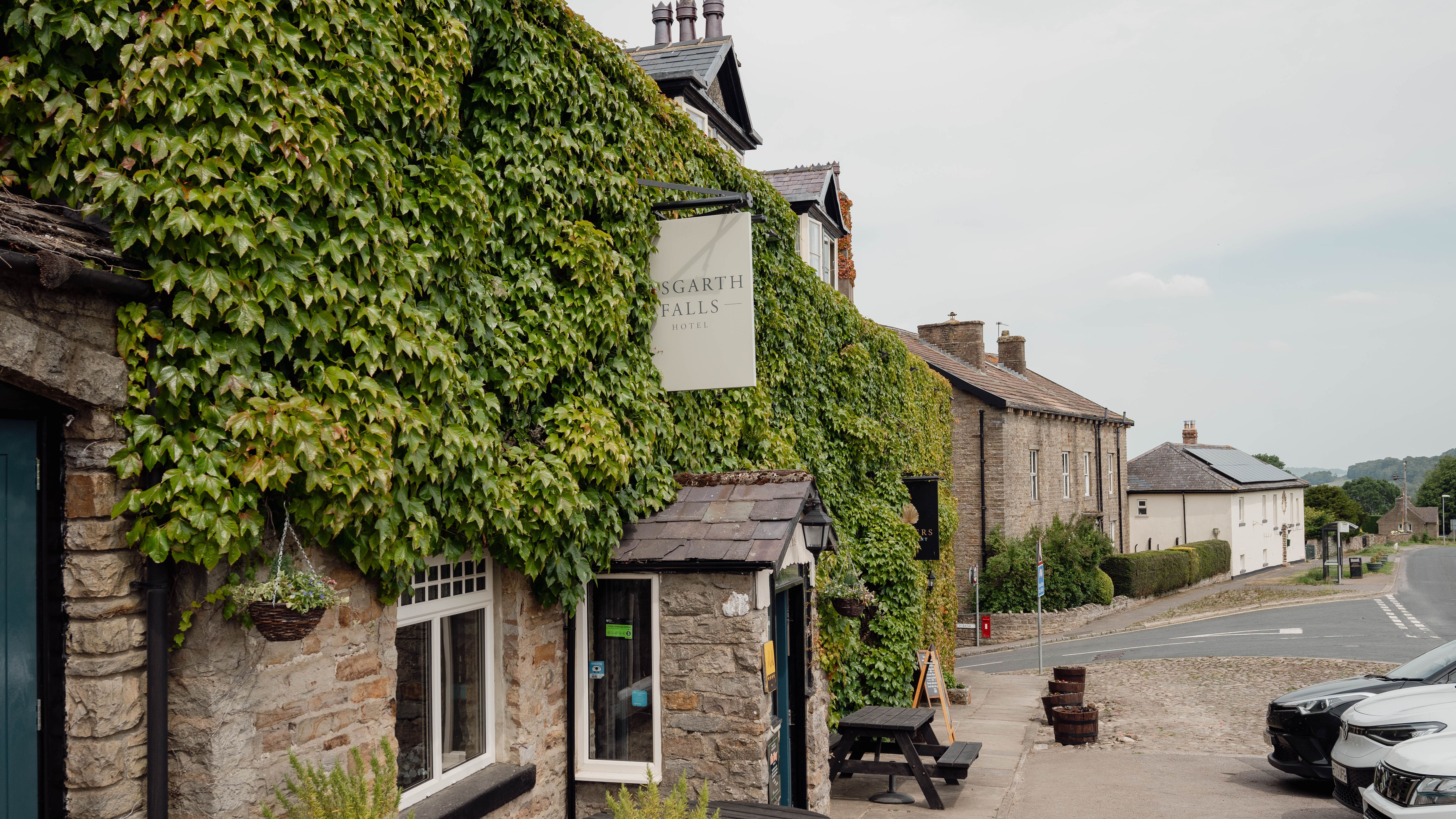 Ivy-covered stone building with outdoor tables on a quiet village street