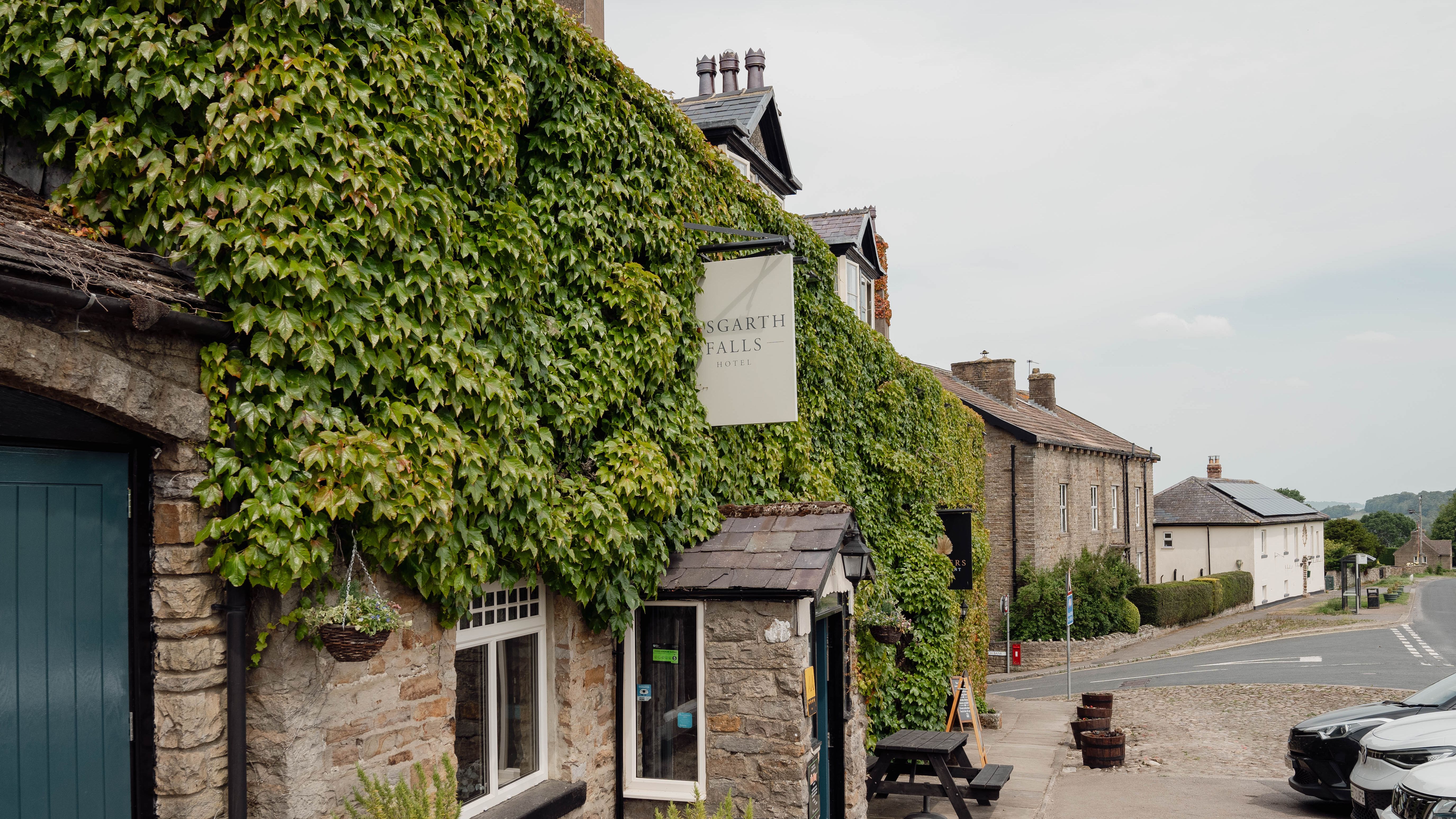 Stone building covered in green ivy on a quiet village street with a sign reading 'Aysgarth Falls Hotel'.